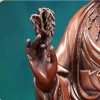 A curled willow sprig held between the fingers of Guanyin’s raised right hand