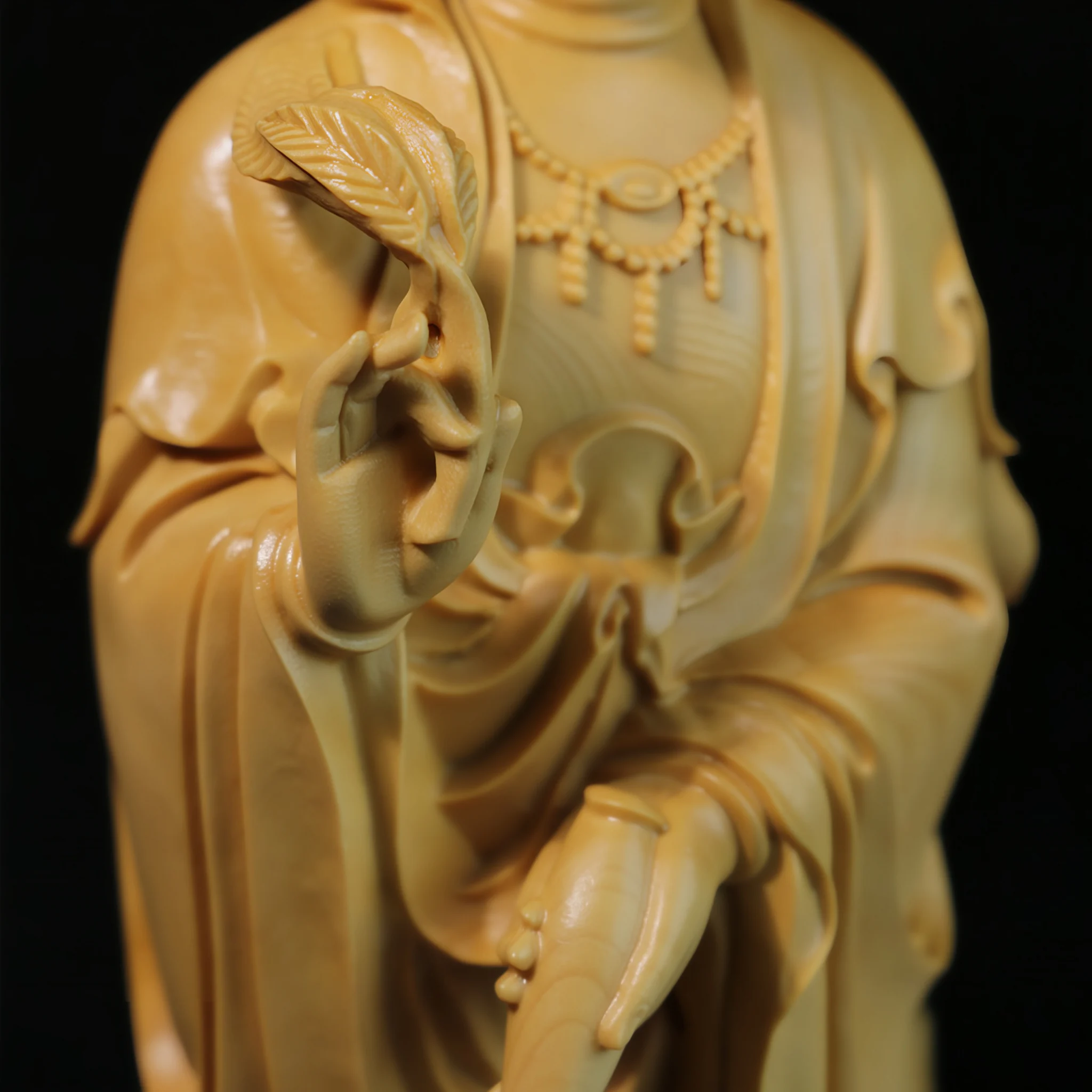 Guanyin’s hand holding a leafy sprig beside the tilted water vase