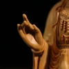 Close view of Guanyin’s raised hand, carved necklace and robe folds in natural boxwood