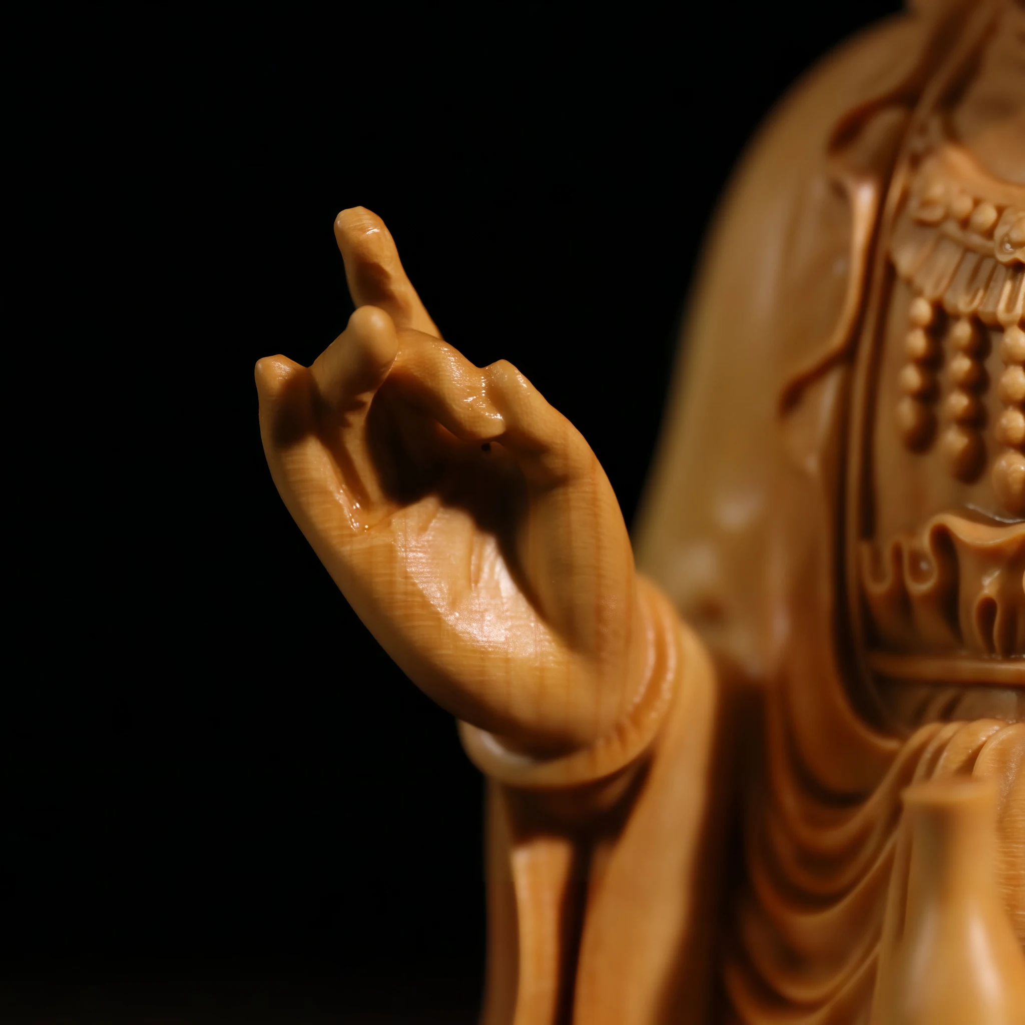 Close view of Guanyin’s raised hand, carved necklace and robe folds in natural boxwood