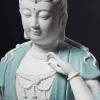 Close-up of the contemplative Kuan Yin statue’s lowered eyes, curved raised fingers, cream-white necklace and finely grained teal robe
