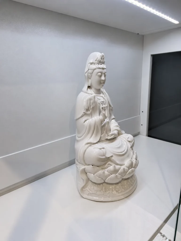The same customer's white porcelain Guanyin seen from the side in its glass cabinet.