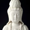 White Kuan Yin face and crown close-up, showing lowered eyes, a small smile and raised ceramic ornament