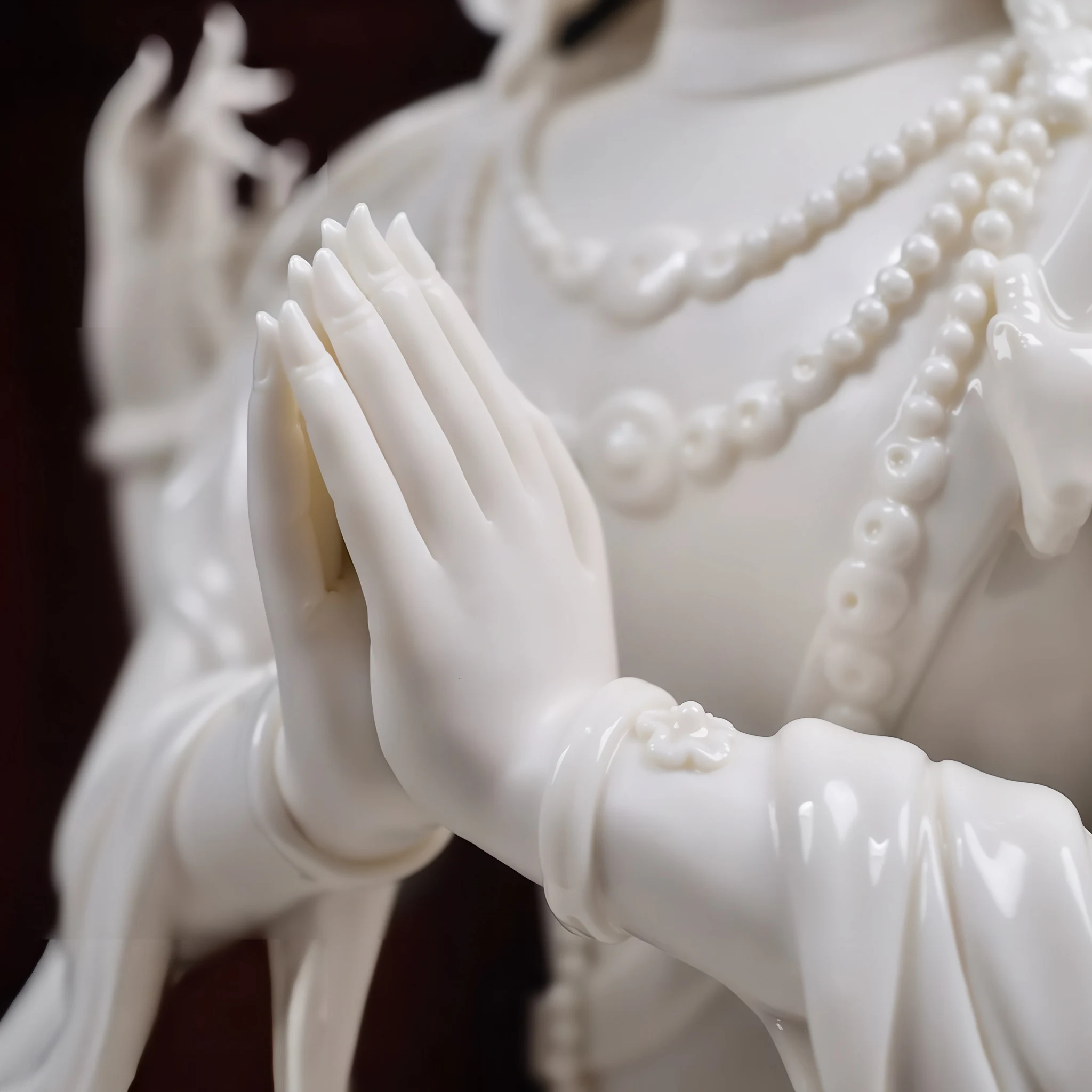 Joined palms and glossy sleeve folds of the white porcelain Four-Armed Guanyin
