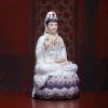 Angled view of a seated Guanyin holding a small vase above a purple and pink lotus base