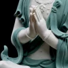 Cream-white joined hands above textured teal robes on the Hezhang Guanyin statue