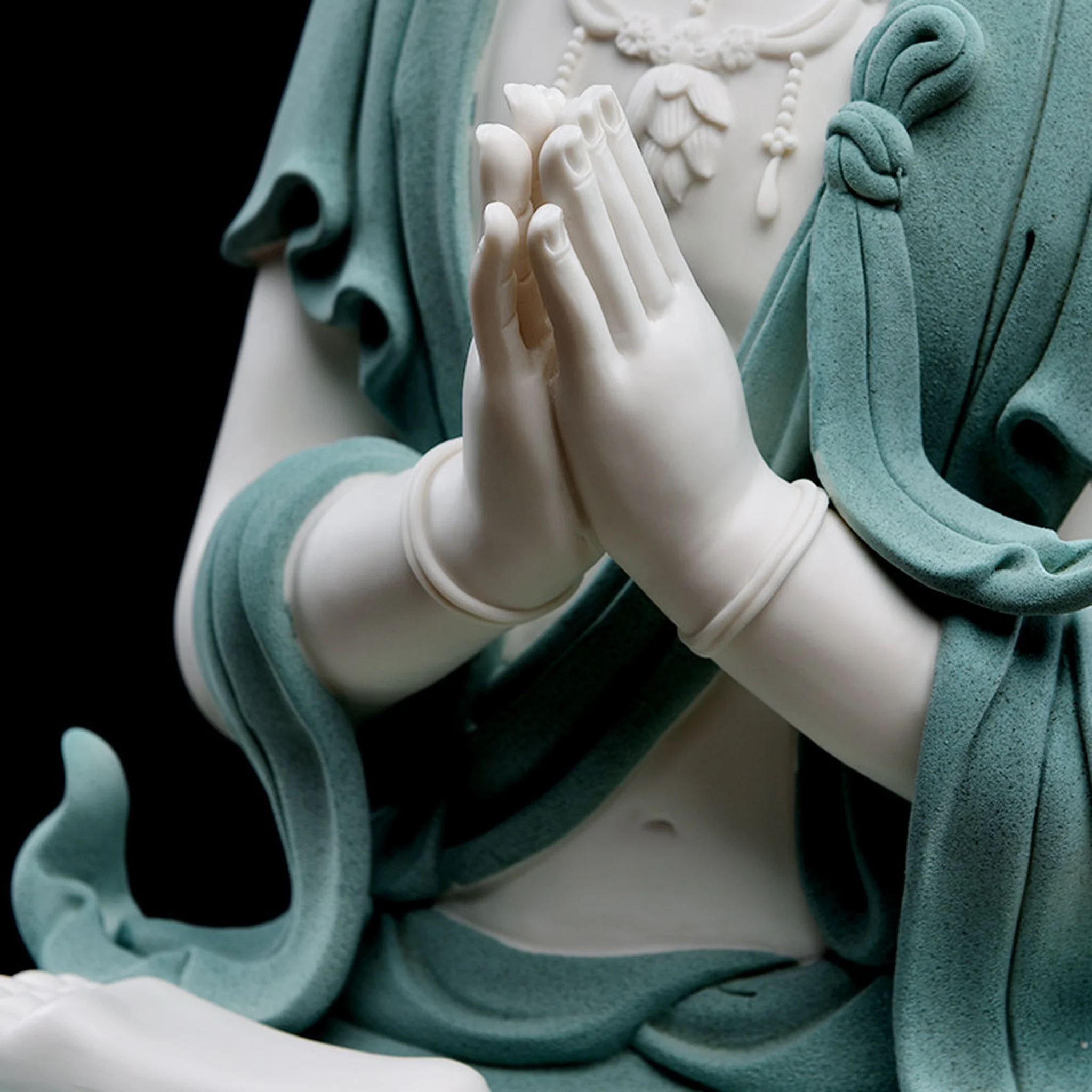 Cream-white joined hands above textured teal robes on the Hezhang Guanyin statue