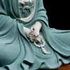 Close-up of the teal Jingsi Guanyin statue’s hands holding sculpted prayer beads and a tassel over textured robes