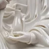 Lower hand of the Kuan Yin statue supporting a slender upright vase, beside the flowing sleeve