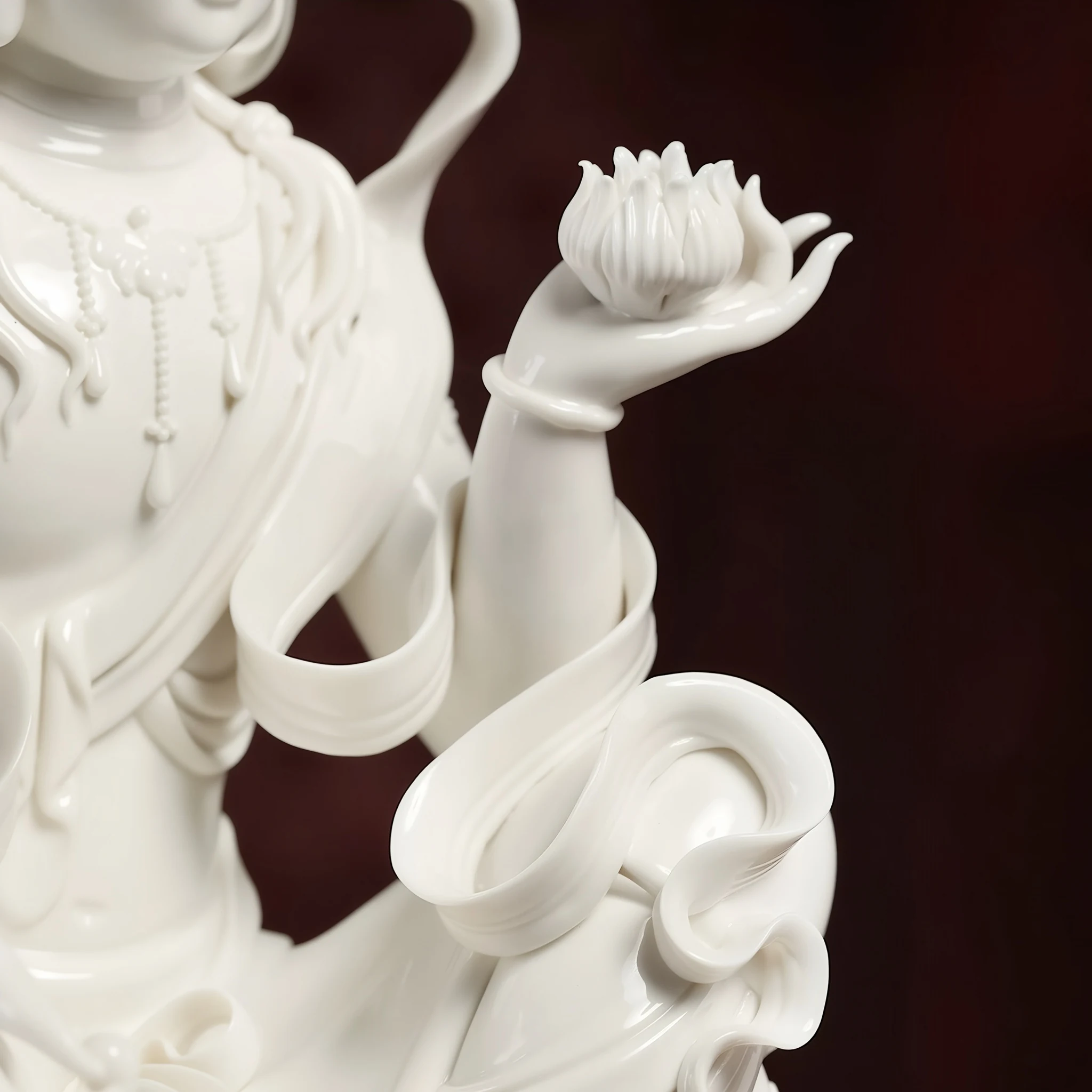 White porcelain Guanyin’s open palm supporting a lotus flower beside curling ribbons and draped sleeves