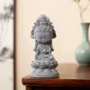 Gray Guanyin figurine displayed on a wooden tabletop beside a background vase