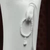 White porcelain hand holding an oval strand of prayer beads with a sculpted tassel