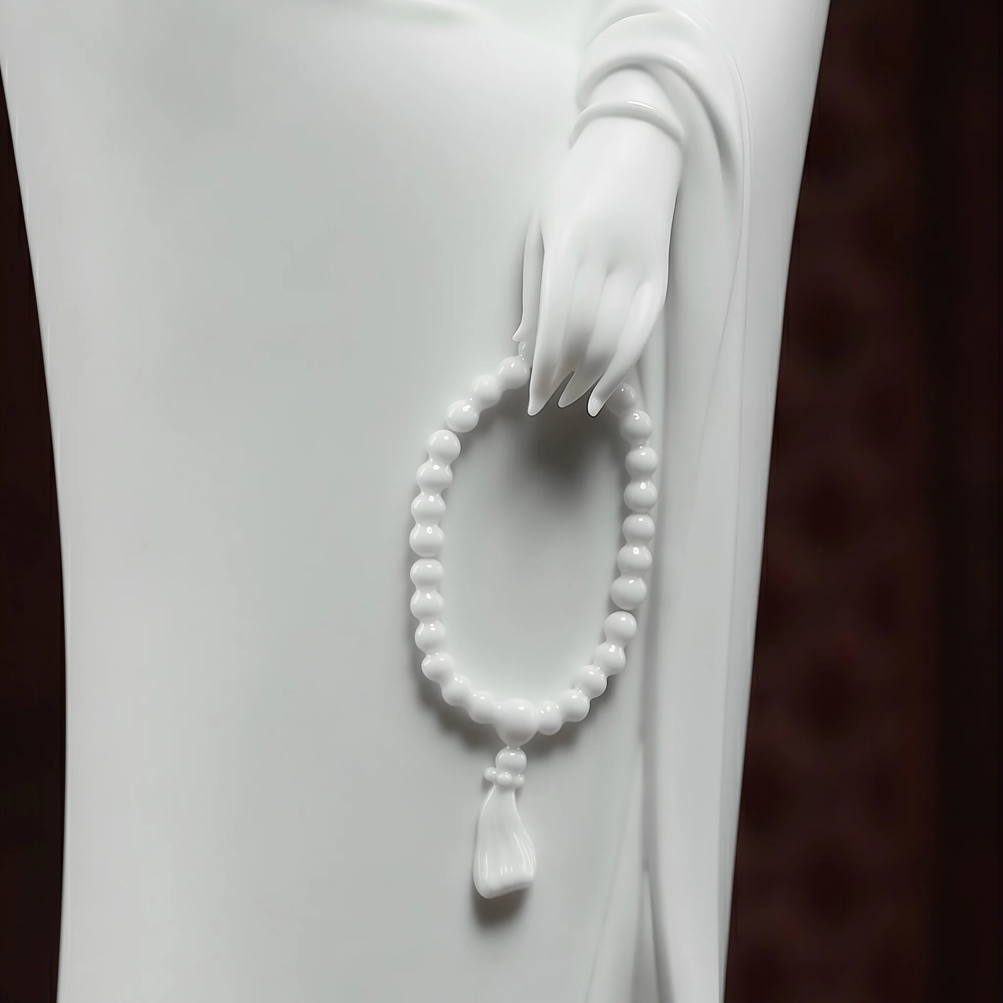 White porcelain hand holding an oval strand of prayer beads with a sculpted tassel