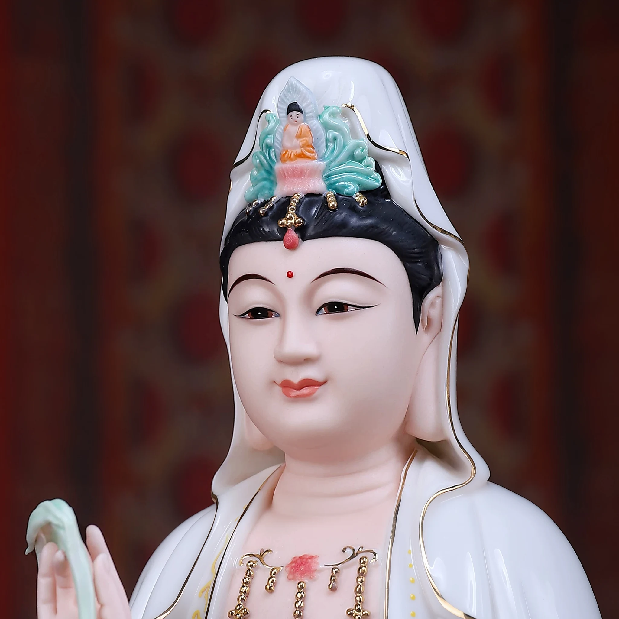 Face and crown detail of a painted porcelain Guanyin statue showing painted face, white veil and turquoise-colored crown details