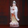 Opposite three-quarter view of a painted porcelain Guanyin statue showing vase, amber-toned gown and raised hand
