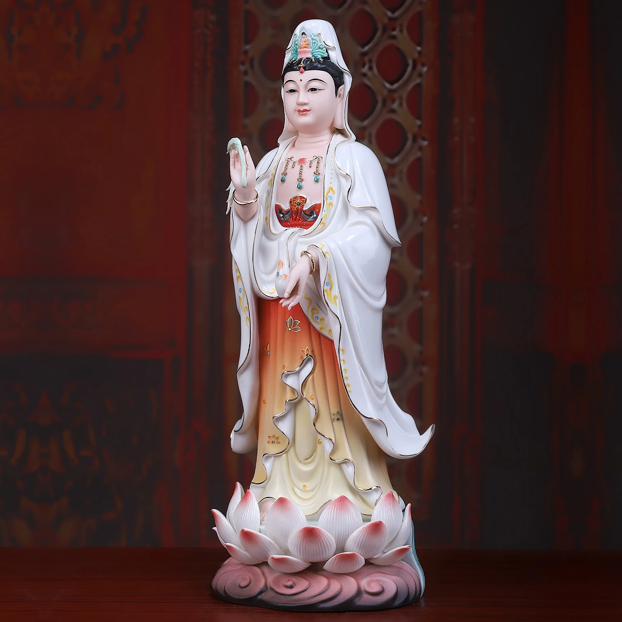 Opposite three-quarter view of a painted porcelain Guanyin statue showing vase, amber-toned gown and raised hand