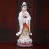 Three-quarter view of a painted porcelain Guanyin statue showing standing figure, flowing white robes and pink lotus base