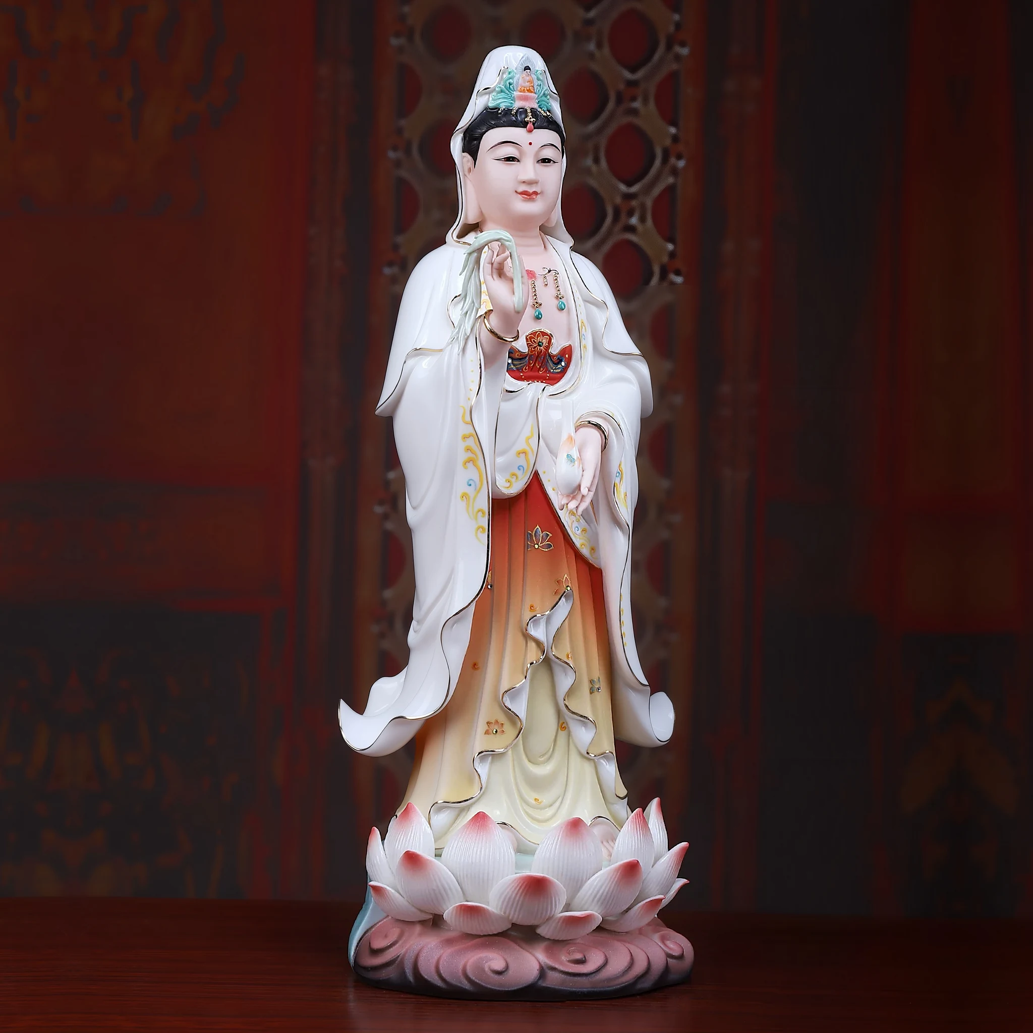 Three-quarter view of a painted porcelain Guanyin statue showing standing figure, flowing white robes and pink lotus base