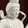 Close-up of Piaodai Kuan Yin’s lowered eyes, small smile, crown and necklace in glazed white porcelain