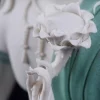 White hand holding a lotus flower beside the speckled teal robes of a Water Moon Guanyin statue
