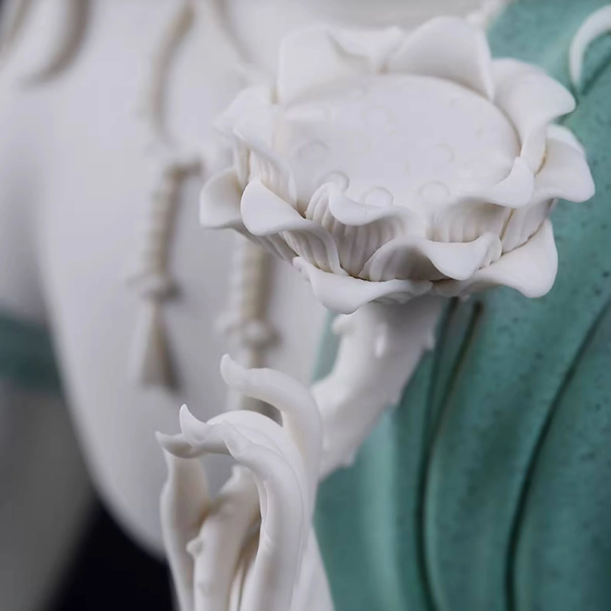 White hand holding a lotus flower beside the speckled teal robes of a Water Moon Guanyin statue