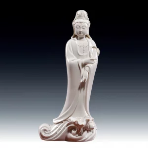Yangzhi Guanyin statue in glossy white ceramic, holding a willow branch and tilted vase above a lotus-leaf and wave base